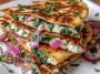 Golden Mediterranean quesadillas filled with spinach, feta, mozzarella, and red onion, cut into wedges and served with fresh herbs.