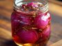 “Jar of vibrant hot honey pickled red onions with a tangy pink hue, served as a topping for tacos.”