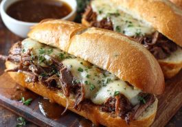 Crockpot French dip sandwich with melted cheese served alongside a bowl of au jus.