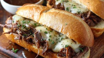 Crockpot French dip sandwich with melted cheese served alongside a bowl of au jus.