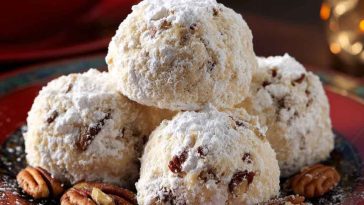 Plate of buttery pecan snowball cookies dusted with powdered sugar.