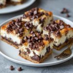 Chocolate chip cheesecake bars with a buttery crust, creamy cheesecake filling, and chocolate chips sprinkled on top, cut into squares and served on a plate.