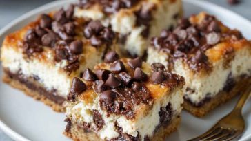 Chocolate chip cheesecake bars with a buttery crust, creamy cheesecake filling, and chocolate chips sprinkled on top, cut into squares and served on a plate.