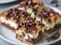 Chocolate chip cheesecake bars with a buttery crust, creamy cheesecake filling, and chocolate chips sprinkled on top, cut into squares and served on a plate.