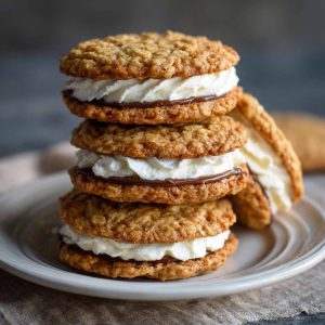 Homemade oatmeal cream pies with soft, chewy oatmeal cookies sandwiched together with a fluffy vanilla cream filling, stacked on a plate for serving.