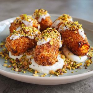 Golden sweet potato croquettes served on a platter with creamy burrata dip, topped with crushed pistachios and fresh herbs, arranged elegantly for a gourmet appetizer.
