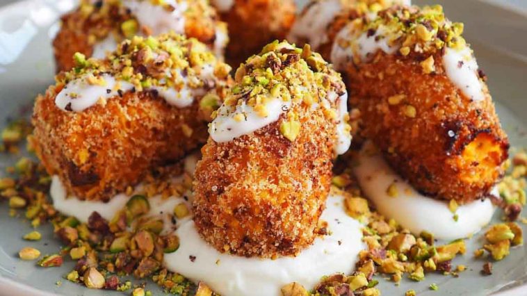 Golden sweet potato croquettes served on a platter with creamy burrata dip, topped with crushed pistachios and fresh herbs, arranged elegantly for a gourmet appetizer.