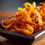 Candied orange peel strips coated in sugar, glistening on a parchment-lined tray, perfect for snacking or dessert garnish.