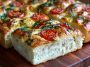 Homemade Margherita focaccia bread baked golden brown, topped with fresh tomatoes, mozzarella, basil leaves, and drizzled with olive oil.