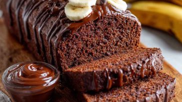 High protein chocolate banana bread sliced on a wooden board, showing moist texture with chocolate chips and protein-rich ingredients, served with a cup of coffee.