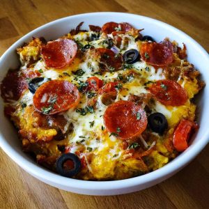 Low carb crustless pizza bowl with melted cheese, pepperoni, and fresh herbs in a dish.