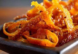 Candied orange peel strips coated in sugar, glistening on a parchment-lined tray, perfect for snacking or dessert garnish.