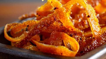 Candied orange peel strips coated in sugar, glistening on a parchment-lined tray, perfect for snacking or dessert garnish.