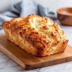 Easy 2-ingredient cottage cheese bread loaf sliced on a wooden board, showing a fluffy texture and golden crust, served with butter and herbs.