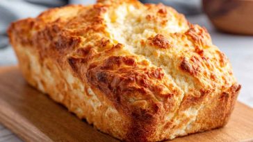 Easy 2-ingredient cottage cheese bread loaf sliced on a wooden board, showing a fluffy texture and golden crust, served with butter and herbs.