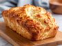 Easy 2-ingredient cottage cheese bread loaf sliced on a wooden board, showing a fluffy texture and golden crust, served with butter and herbs.
