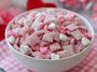 Valentine’s Day muddy buddies coated in pink and red sprinkles, powdered sugar, and chocolate, served in a festive bowl with heart-shaped decorations.