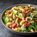 Big Mac Pasta Salad with ground beef, cheddar cheese, lettuce, pickles, and creamy special sauce in a colorful bowl.