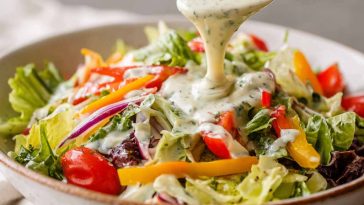 Best ever creamy Italian salad dressing in a glass jar, made with mayonnaise, olive oil, vinegar, garlic, herbs, and Parmesan cheese, served alongside a fresh green salad.