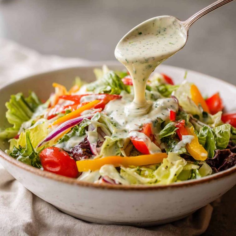 Best ever creamy Italian salad dressing in a glass jar, made with mayonnaise, olive oil, vinegar, garlic, herbs, and Parmesan cheese, served alongside a fresh green salad.