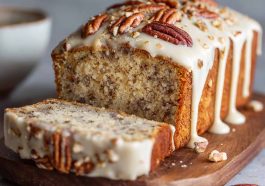 Butter pecan cake loaf topped with rich cream cheese icing, garnished with chopped pecans, served on a rustic wooden board.