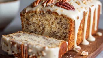 Butter pecan cake loaf topped with rich cream cheese icing, garnished with chopped pecans, served on a rustic wooden board.