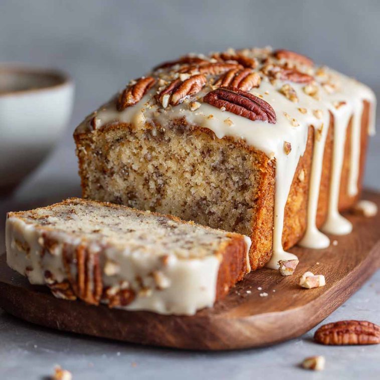 Butter pecan cake loaf topped with rich cream cheese icing, garnished with chopped pecans, served on a rustic wooden board.