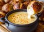 Creamy beer cheese dip served in a bowl, golden and smooth, topped with chives, surrounded by pretzels, chips, and fresh vegetables for dipping.