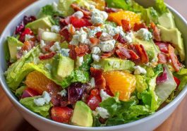 Homemade Ruth’s Chris chopped salad with iceberg lettuce, spinach, red onions, mushrooms, hearts of palm, bacon, and croutons tossed in lemon basil dressing, served in a large bowl.