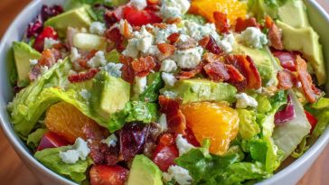 Homemade Ruth’s Chris chopped salad with iceberg lettuce, spinach, red onions, mushrooms, hearts of palm, bacon, and croutons tossed in lemon basil dressing, served in a large bowl.