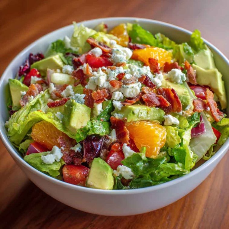 Homemade Ruth’s Chris chopped salad with iceberg lettuce, spinach, red onions, mushrooms, hearts of palm, bacon, and croutons tossed in lemon basil dressing, served in a large bowl.