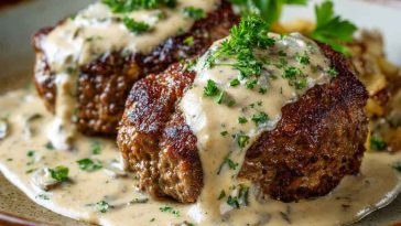 Juicy hamburger steaks smothered in creamy whiskey sauce, served with mashed potatoes and garnished with fresh herbs on a rustic plate.