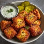Golden crispy cheese bites with tangy pickles inside, served on a platter.