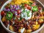 Loaded potato taco bowl filled with crispy roasted potatoes, seasoned ground beef, cheese, salsa, sour cream, and fresh toppings like lettuce and jalapeños, served in a rustic bowl.