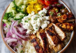 Greek chicken bowl with marinated chicken, rice, cucumber, tomato, olives, and tzatziki sauce.