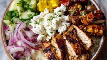 Greek chicken bowl with marinated chicken, rice, cucumber, tomato, olives, and tzatziki sauce.