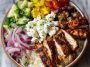 Greek chicken bowl with marinated chicken, rice, cucumber, tomato, olives, and tzatziki sauce.