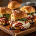 Hot Italian sub sliders baked golden brown with layers of salami, pepperoni, ham, melted cheese, and Italian seasoning, served on slider buns with a buttery glaze.