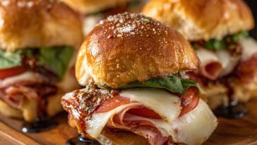 Hot Italian sub sliders baked golden brown with layers of salami, pepperoni, ham, melted cheese, and Italian seasoning, served on slider buns with a buttery glaze.