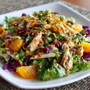 Asian chicken cranberry salad served in a large bowl with shredded chicken, crisp cabbage, carrots, dried cranberries, toasted almonds, and sesame dressing, garnished with green onions.