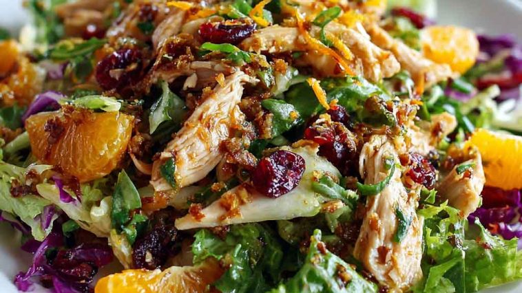 Asian chicken cranberry salad served in a large bowl with shredded chicken, crisp cabbage, carrots, dried cranberries, toasted almonds, and sesame dressing, garnished with green onions.