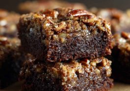 Pecan pie brownies with a fudgy chocolate base topped with gooey pecan pie filling, baked golden brown and sliced into squares, garnished with extra pecans.