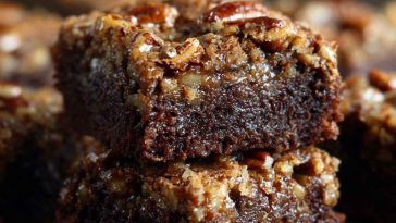 Pecan pie brownies with a fudgy chocolate base topped with gooey pecan pie filling, baked golden brown and sliced into squares, garnished with extra pecans.