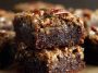 Pecan pie brownies with a fudgy chocolate base topped with gooey pecan pie filling, baked golden brown and sliced into squares, garnished with extra pecans.