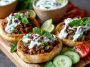Mediterranean mini lahmacun bites topped with spiced ground meat, fresh herbs, and drizzled with creamy yogurt sauce, served on a platter as an appetizer.