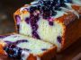 Blueberry cream cheese loaf with golden crust, swirled cream cheese filling, and fresh blueberries, sliced and served on a wooden board.