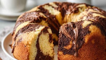Soft and moist marble cake sliced to reveal swirls of vanilla and chocolate, served on a wooden board with a dusting of powdered sugar.