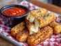 Nashville Hot Mozzarella Stick coated in spicy crispy crust, golden brown, served with a side of dipping sauce.
