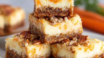 Cream cheese bars with carrot cake flavor, topped with creamy frosting and sprinkled with cinnamon, served on a tray with fresh carrot shavings.