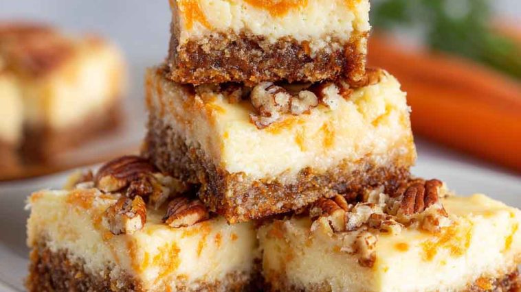Cream cheese bars with carrot cake flavor, topped with creamy frosting and sprinkled with cinnamon, served on a tray with fresh carrot shavings.